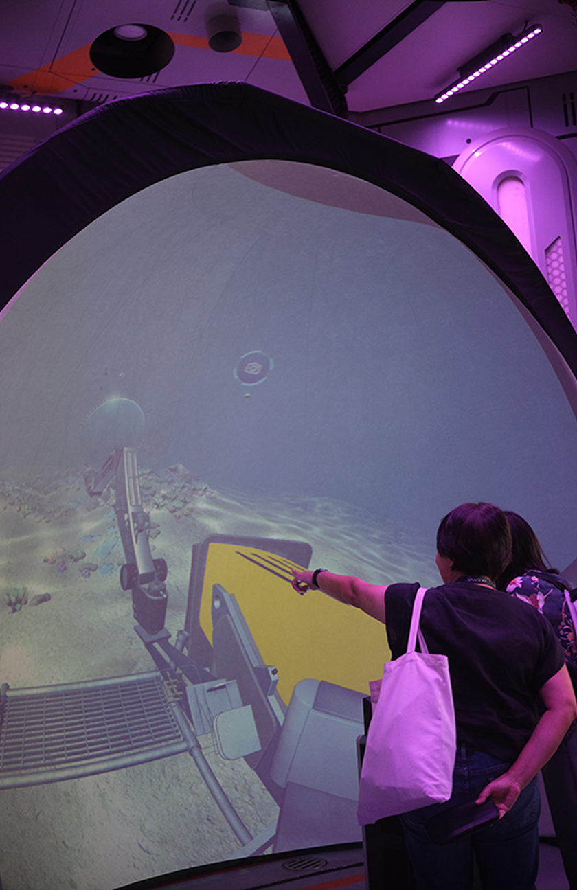 Siti Nurbaya standing beside the dome installation at the live showcase, with the submersible simulation visible on screen behind her.